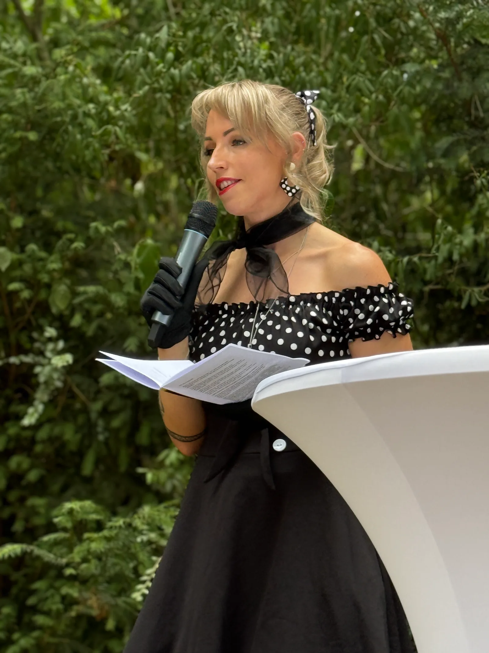 Nadine Butz, freie Traurednerin, spricht bei einer freien Trauung ins Mikrofon vor grünem Blätterhintergrund